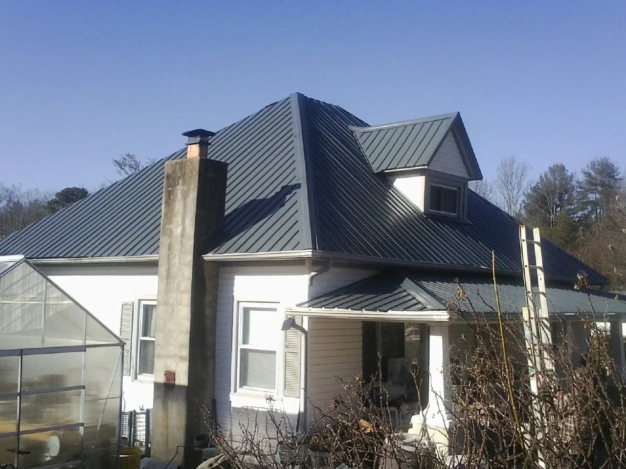 Dark blue standing seam metal roof on a white farmhouse with dormer in Reno