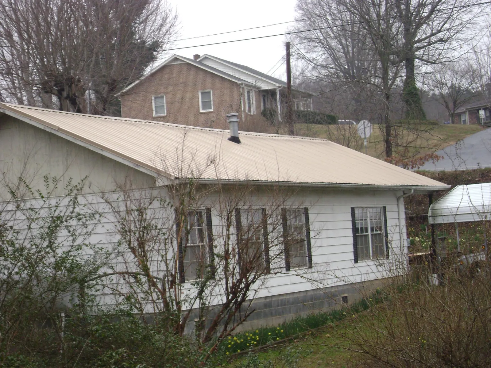 Tan metal roof on a white sided house set into a hillside — Commercial Roofing by Roofing Brothers in Reno